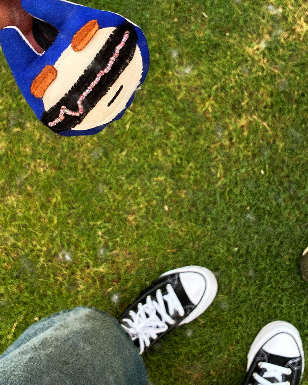 Blue keychain against denim, sneakers and grass
